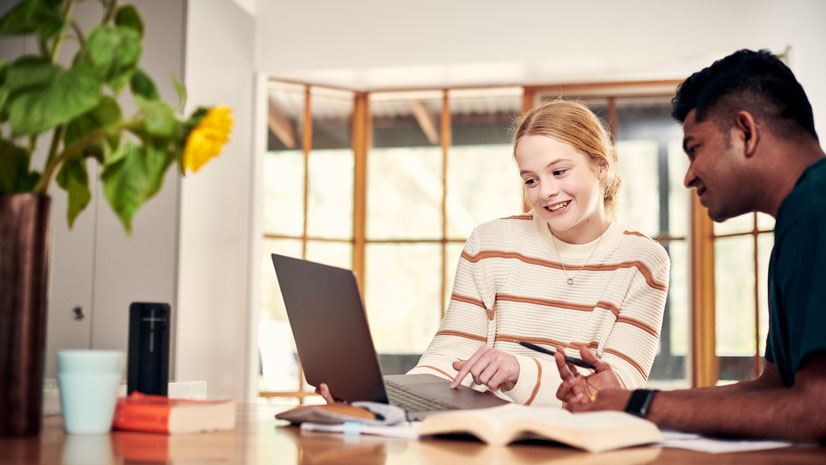 Image of two students talking and studying while looking at a laptop