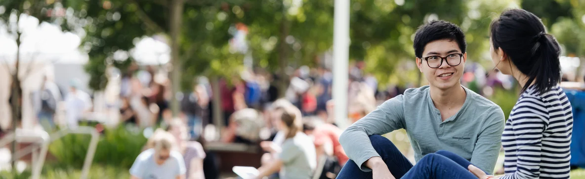 Deakin international students talking outside, sitting on grass.