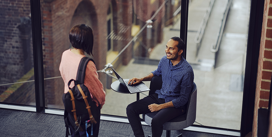 Two students talking, one is standing and one is sitting