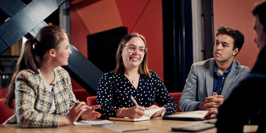 Internship students sit around a table listening to the person in the centre who is smiling 
