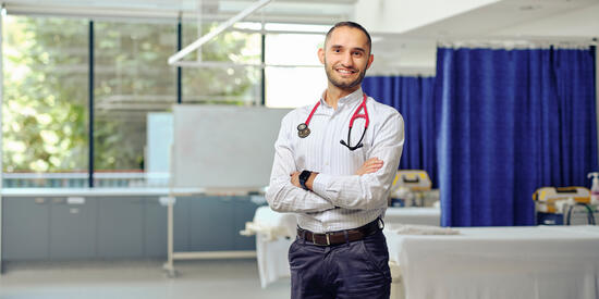 Deakin Doctor standing with arms crossed and smiling in a clinical setting.