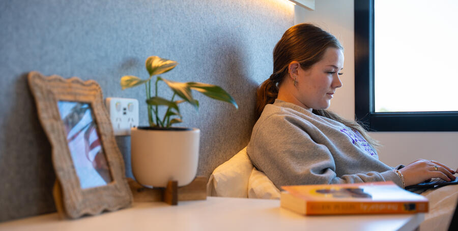 A resident using their laptop in bed at Geelong Waurn Ponds on-campus accommodation.