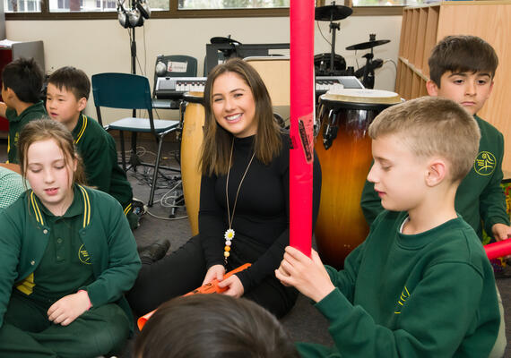 A Deakin psychology student sits on the floor amongst young children smiling at the camera
