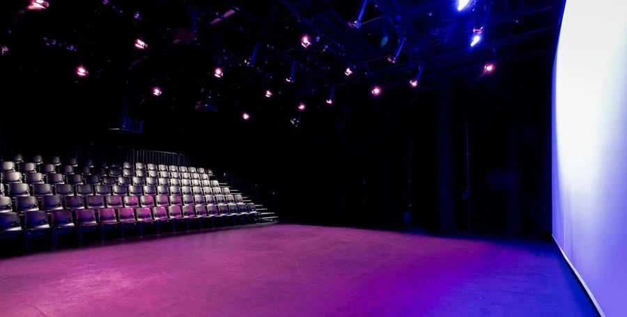 Large black box style theatre, taken from the wings, showing size of stage and projection screen, and lighting on