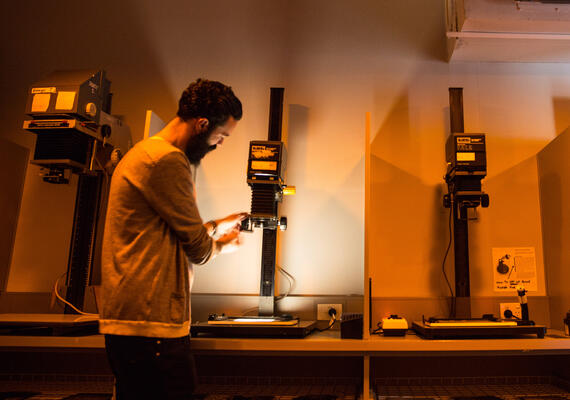 Wide-angle shot of a creative arts and photography student using a black and white enlarger with a filter to develop photographs.
