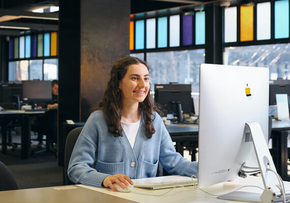 A student in a blue cardigan at a desktop computer.