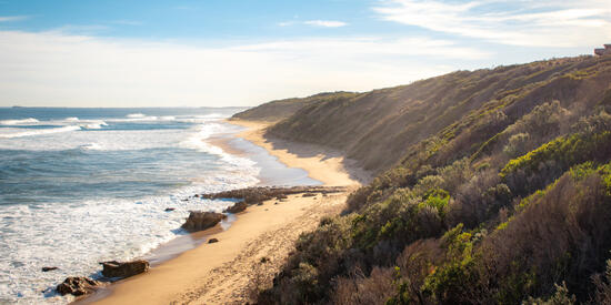 A beach with a cliff and crashing waves.