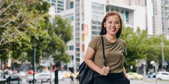 Deakin student standing in Melbourne park smiling with bag.