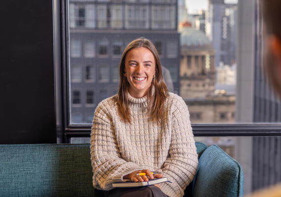 A Deakin Law student smiles on a couch balancing a notebook on their knee