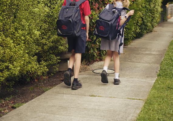 Two children wearing school uniforms and school bags walking to school.