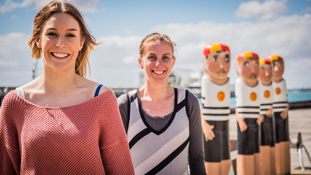 Two people standing at the Geelong Waterfront in front of the bollards.