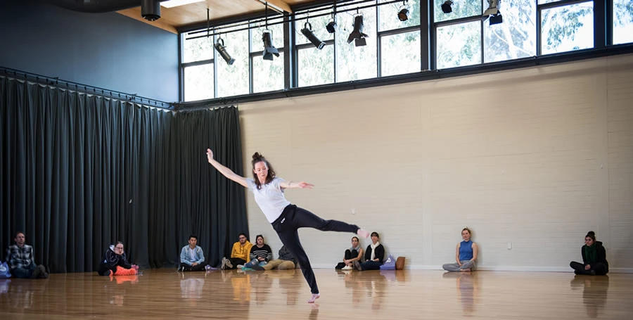 One dancer performing while open day visitors sit on polished floor boards and watch in light filled studio