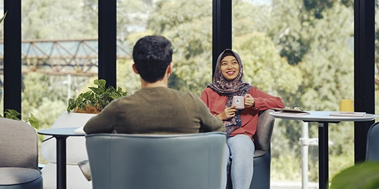 Two international students sit chatting. One is holding a mug.
