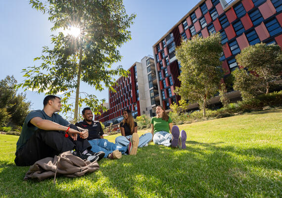Four student residents sitting on the grass with on-campus accommodation in background.