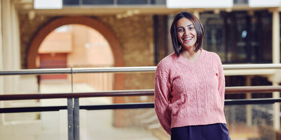 A postgraduate student in a pink top stands on a balcony at the Geelong Waterfront Campus.