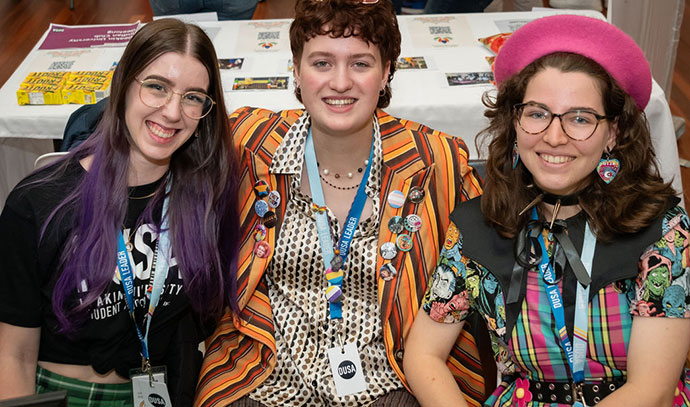 visual-story Three Deakin students in colourful clothing at a DUSA welcome desk