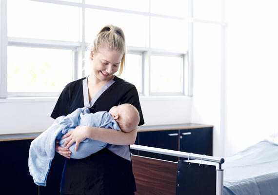 A nurse stands in a hospital cradling a baby.