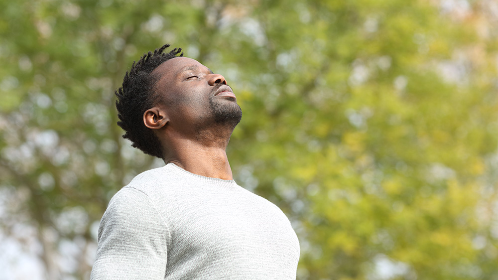 A person standing outside inhaling deeply, eyes closed