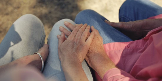 Two people sitting on a park bench and holding hands.