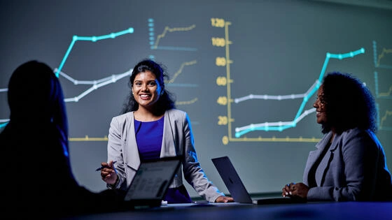 Three postgraduate digital finance Deakin students inside classroom with data graphs on a presentation screen.