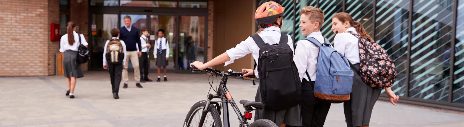 Three school students work into school, one is pushing a bike. 