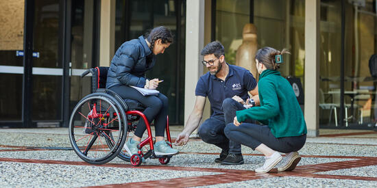 Person in a wheelchair chatting to two occupational therapists at Deakin Waterfront Campus.