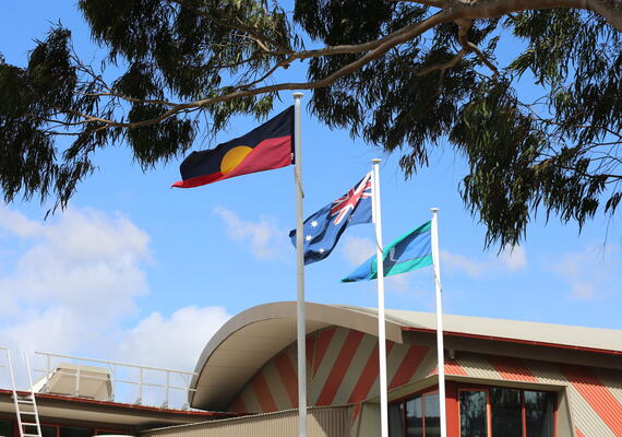 The Aboriginal flag, the Australian flag and the Torres Strait Islander flag all stand outside.