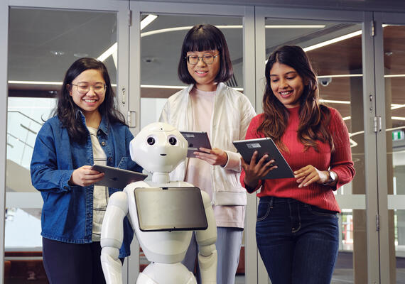 Three Deakin students with a robot looking at tablets in a campus lab.