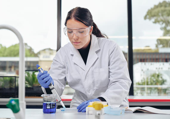 Deakin student in a lab coat performing scientific research.