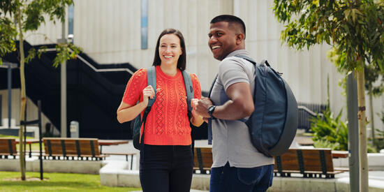 Two Deakin students on campus outside, one is looking over their shoulder.