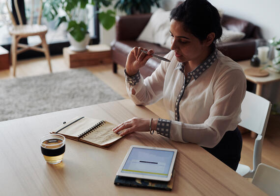 A person sits at a table with a notebook and ipad.