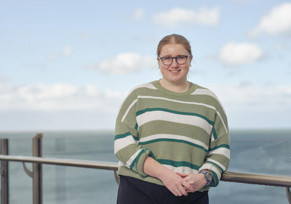 A Deakin student standing on a balcony at the waterfront campus, with the harbour behind her.