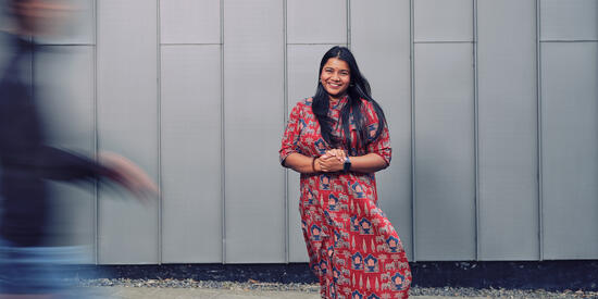 A postgraduate student stands in front of a grey wall outside the Law School Building.