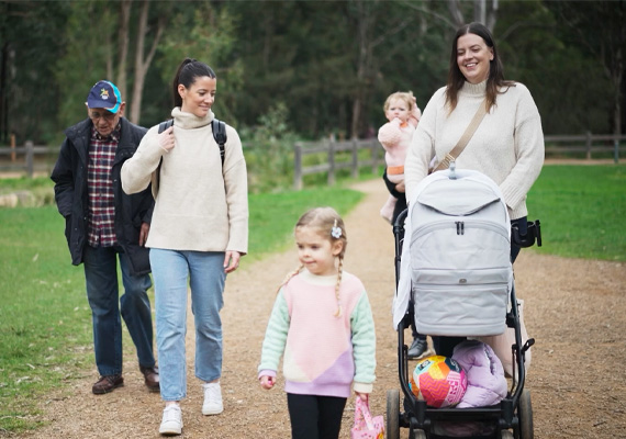 A family walk outside together, one person is pushing a pram and two children walk ahead.