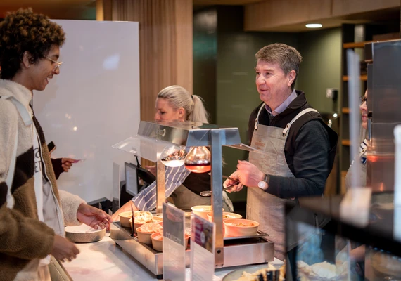 Deakin Caretaker VC Matthew Clarke stands behind a cafe counter serving lunch meals to students
