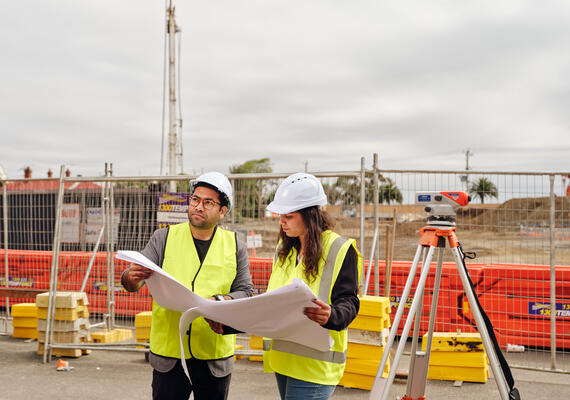Two construction workers wearing hard hats work outside on site.