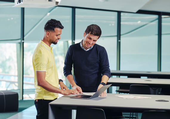 Two students stand looking at a laptop.