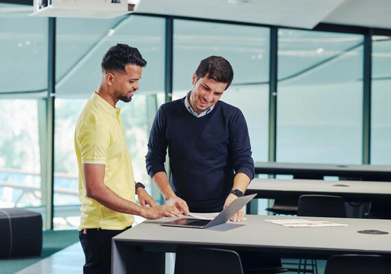 Two students stand looking at a laptop.