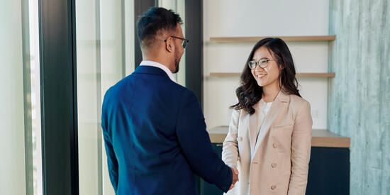 Two people shaking hands inside a corporate office building.