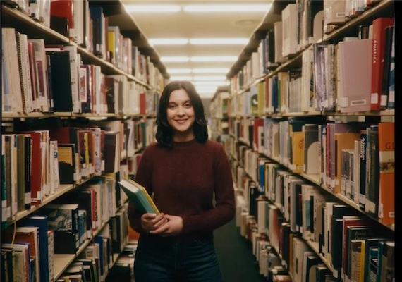 Deakin Alumni student in the Deakin library amongst books.