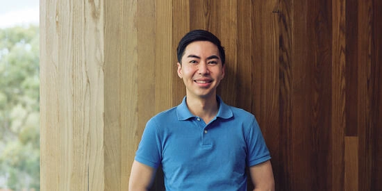 A Deakin international student leans against a wooden wall and smiles at the camera