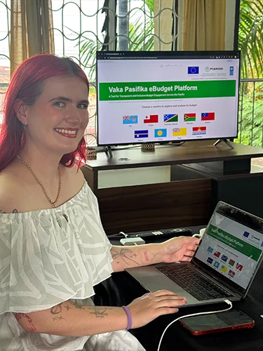 Sarah sitting next to a computer with the Vaka Pasifika eBudget Platform open