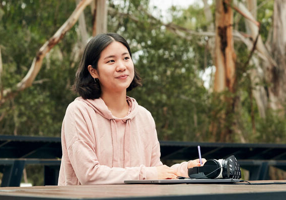 Student smiles while sitting and studying outside at Burwood Campus.