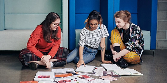 Three Deakin arts students sit on the floor looking at learning materials.