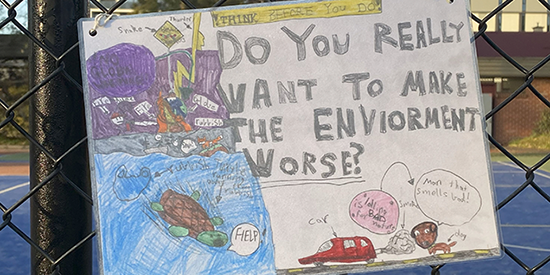 A poster drawn by a child with an illustration urging adults to turn off their cars while waiting  at schools.
