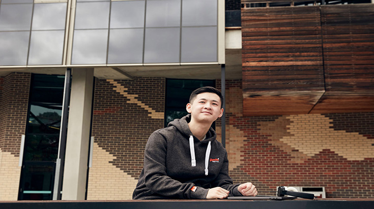 A student sitting outside, looking contemplative.