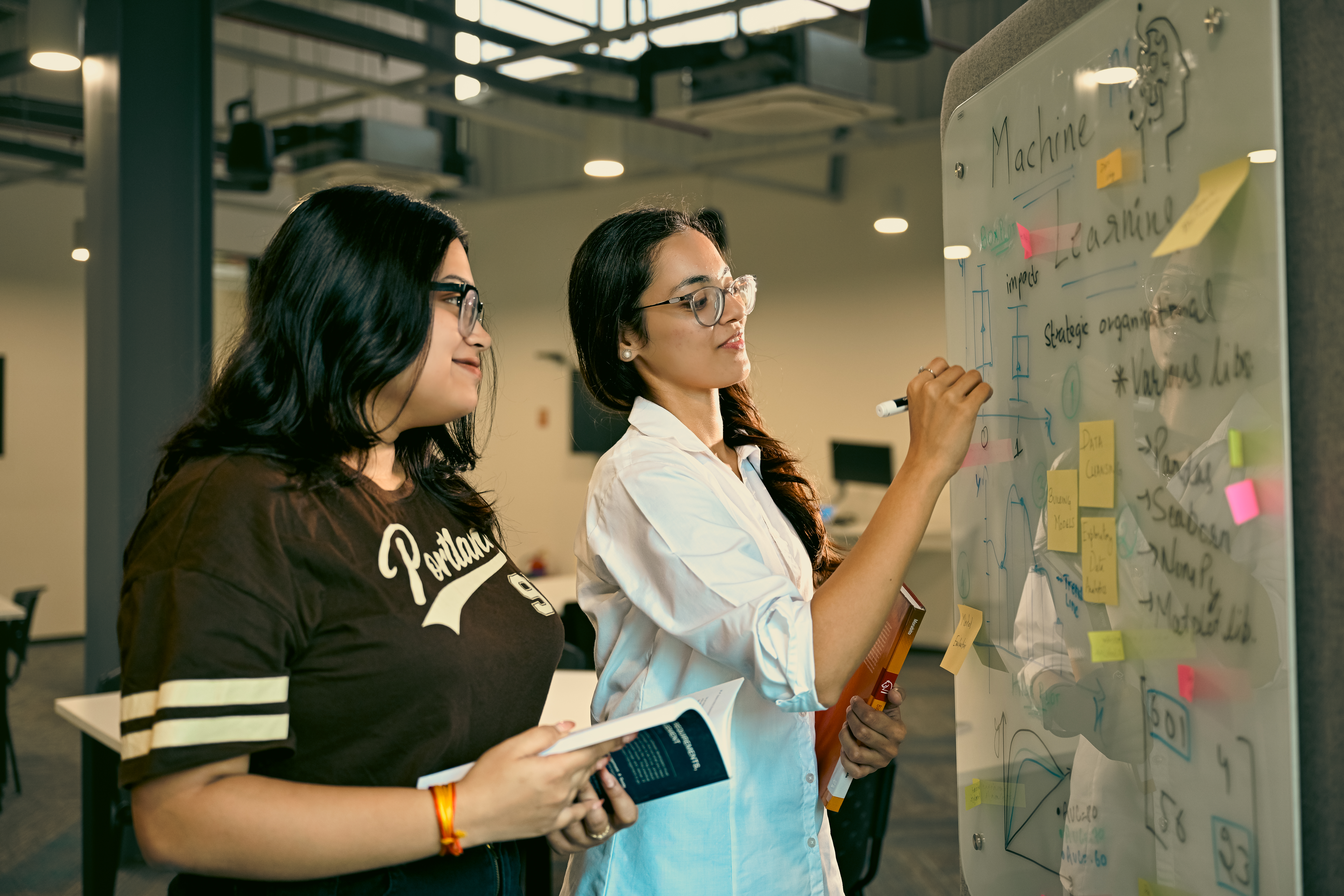 Two Deakin students write on a whiteboard.