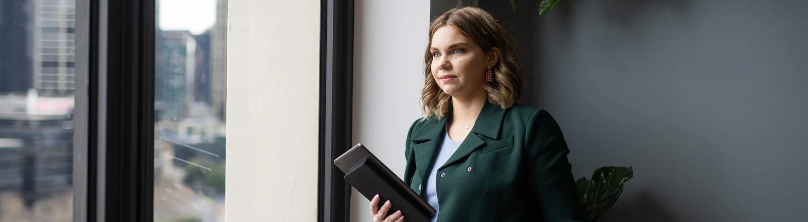 A Deakin business student stands looking out of a window holding a tablet