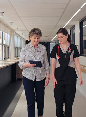 Two health professionals walk together in a hospital hallway.