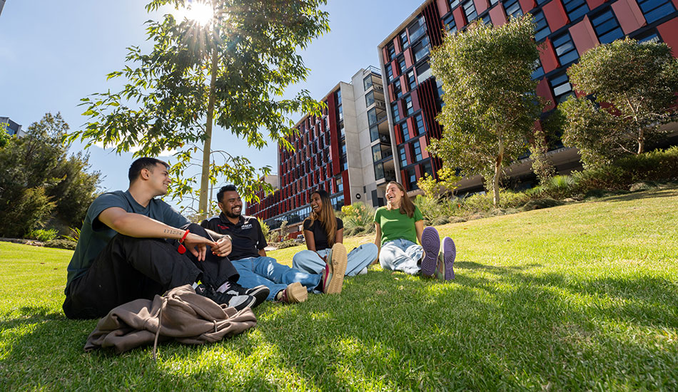 4 residents sitting on the grass with on-campus accommodation in background